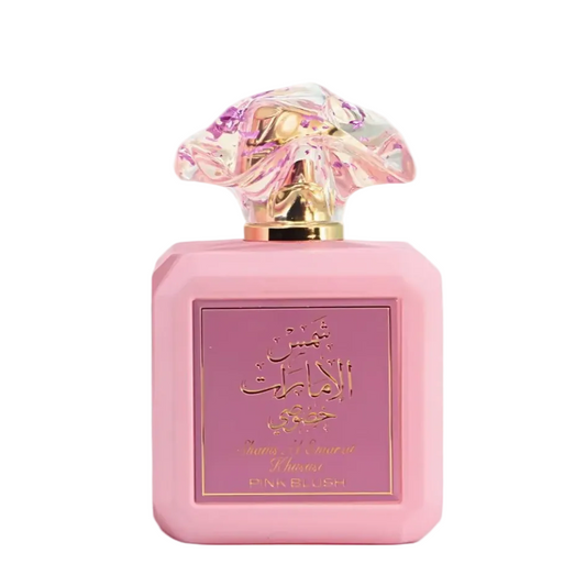 Pink perfume bottle with a pink label featuring gold Arabic calligraphy and 'PINK BLUSH' text, topped with a sculpted iridescent cap on a white background.